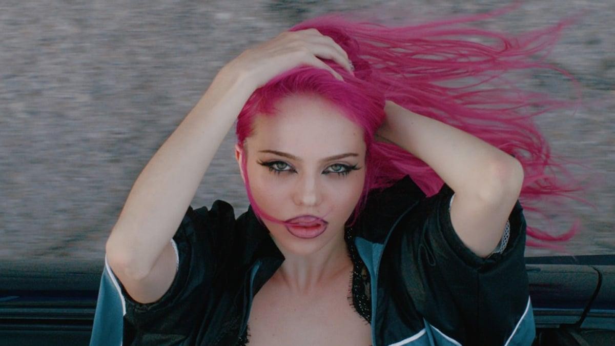 Adéla with bright pink hair, hands in her hair, in a still from the 'Ain't In LA' music video